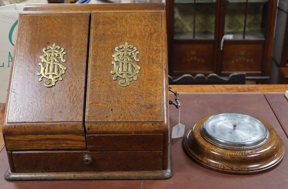 An oak stationery cabinet with brass monograms, 39 x 36cm, together with an oak aneroid barometer